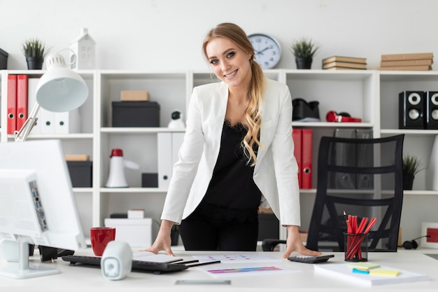 Uma jovem mulher fica no escritório perto de uma mesa de computador.