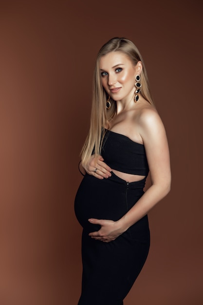 Uma jovem mulher grávida em um vestido está de pé sobre um fundo marrom. foto tirada em um estúdio de fotografia