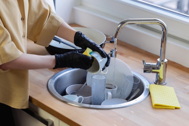 Uma jovem mulher limpa na cozinha, lavando a louça. Ela está cansada e não satisfeita com o fato de que precisa fazer isso.