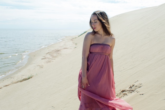 Uma jovem mulher linda em um vestido rosa caminha sobre as dunas de areia