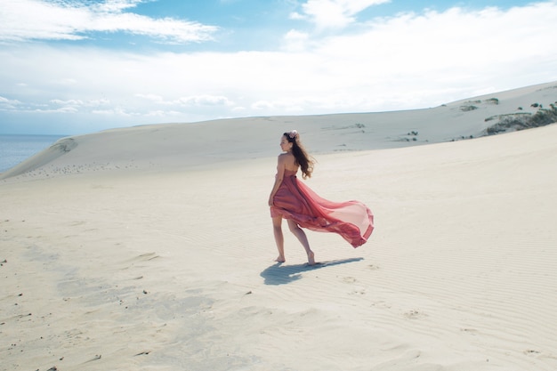 Uma jovem mulher linda em um vestido rosa caminha sobre as dunas de areia