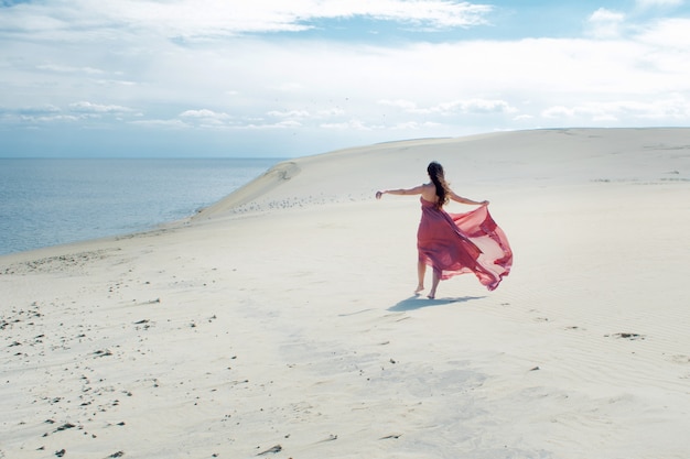 Uma jovem mulher linda em um vestido rosa caminha sobre as dunas de areia
