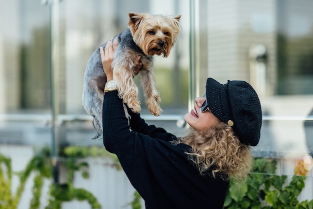 Uma jovem mulher loira de cabelos brancos segura um pequeno cachorro engraçado nos braços de duas cores de chihuahua preto e branco. Abraços e beijos amor.