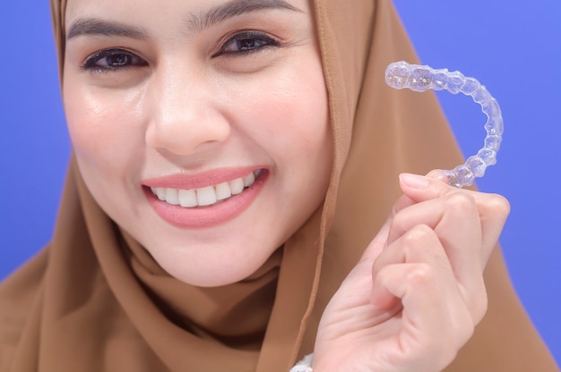 Uma jovem mulher muçulmana segurando o aparelho invisalign em estúdio, atendimento odontológico e conceito ortodôntico.