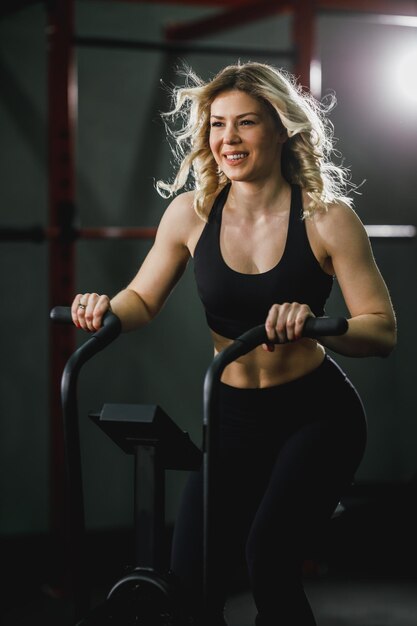 Uma jovem mulher musculosa está fazendo treinamento de crossfit de bicicleta hard cal no ginásio.