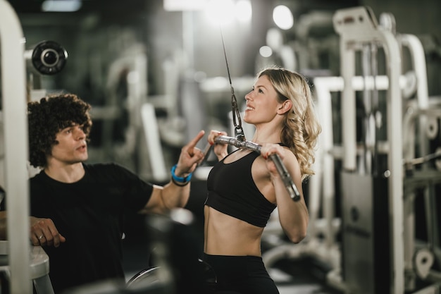 Uma jovem mulher musculosa está treinando na máquina de apoio pelo treinador no ginásio.