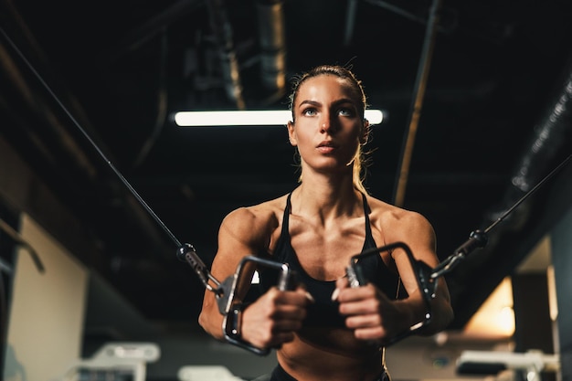 Uma jovem mulher musculosa fazendo treinamento duro para os músculos do peito no ginásio.