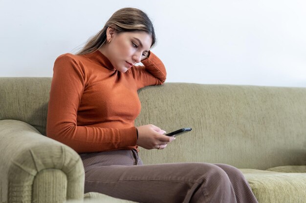 Foto uma jovem mulher olhando para o seu telemóvel sentada num sofá