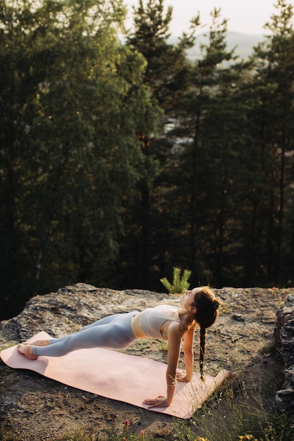 Foto uma jovem mulher pratica ioga nas montanhas contra o fundo de uma floresta de pinheiros