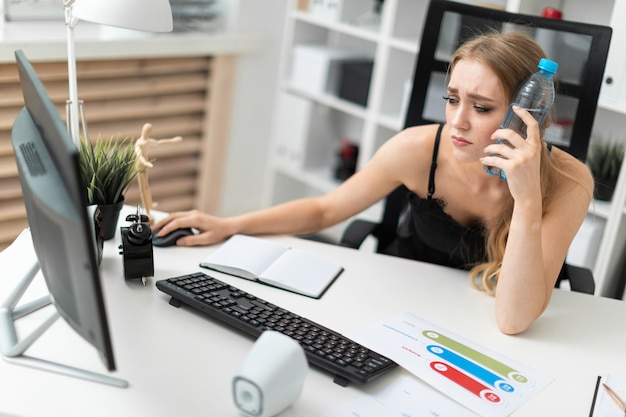 Uma jovem mulher se senta em uma mesa de computador no escritório e coloca uma garrafa de água na cabeça.