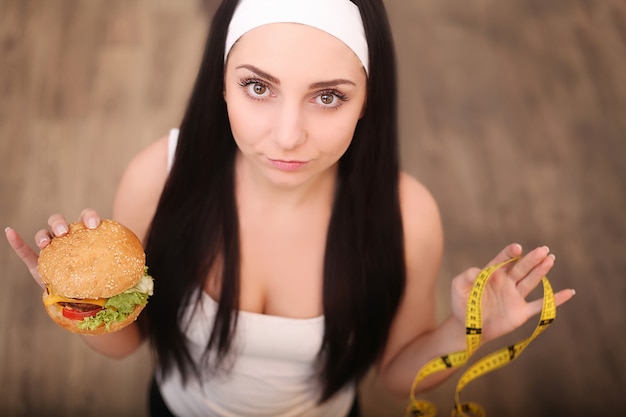 Foto uma jovem mulher segurando um hambúrguer e uma fita métrica. uma garota fica em um de madeira. a vista do topo. o de uma alimentação saudável.