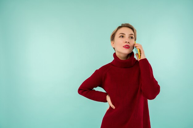 Uma jovem mulher séria com um suéter vermelho e um smartphone em um fundo azul