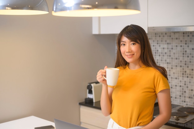 Uma jovem mulher trabalhando com seu laptop e tomando uma xícara de café, estilo de vida e conceito de negócio