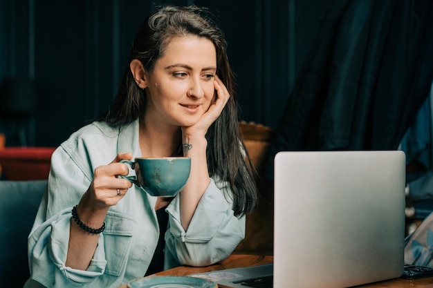 Uma jovem mulher trabalhando em um laptop em um café bebendo café e desfrutando