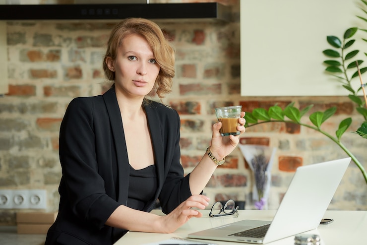 Foto uma jovem mulher trabalhando remotamente em sua cozinha. uma chefe mulher tomando café antes de uma videoconferência com seus funcionários em casa.