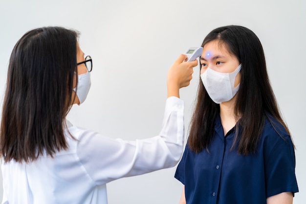 Uma jovem mulher usando máscara facial usando o verificador de temperatura portátil para verificar a temperatura de outra jovem mulher usando máscara facial