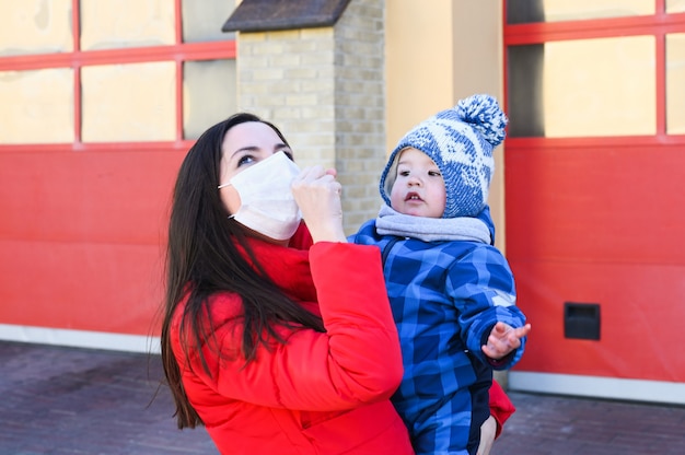 Uma jovem mulher vestindo uma máscara facial e segurando nas mãos um garotinho. medidas protetoras. mãe e filho em quarentena.