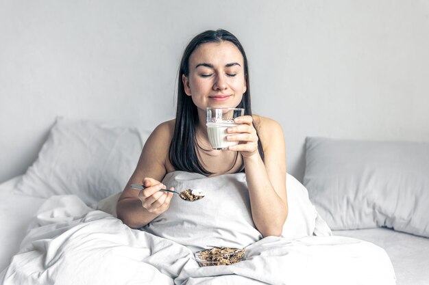 Uma jovem na cama branca com cereais e leite