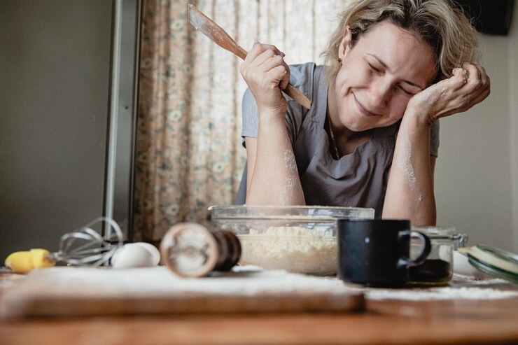 Uma jovem na cozinha com uma espátula nas mãos na frente de uma tigela está chateada por não saber cozinhar