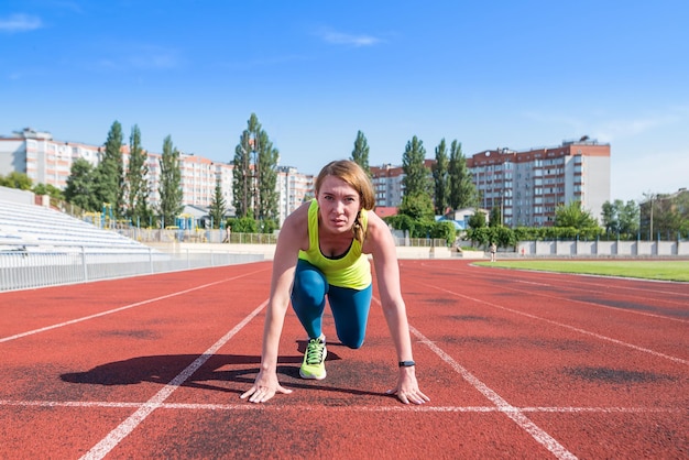 Uma jovem na posição inicial para correr em uma pista de esportes desportista no início