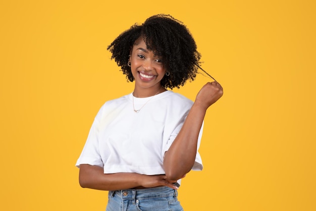 Uma jovem negra encaracolada positiva em camiseta branca toca flertes de cabelo