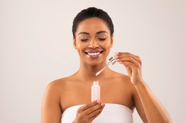 Uma jovem negra sorridente e atraente a aplicar sérum facial.