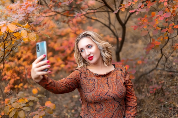 Uma jovem no fundo de um parque de outono tira uma selfie em seu telefone