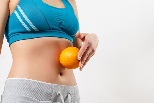 Uma jovem no sportswear detém uma laranja no estômago