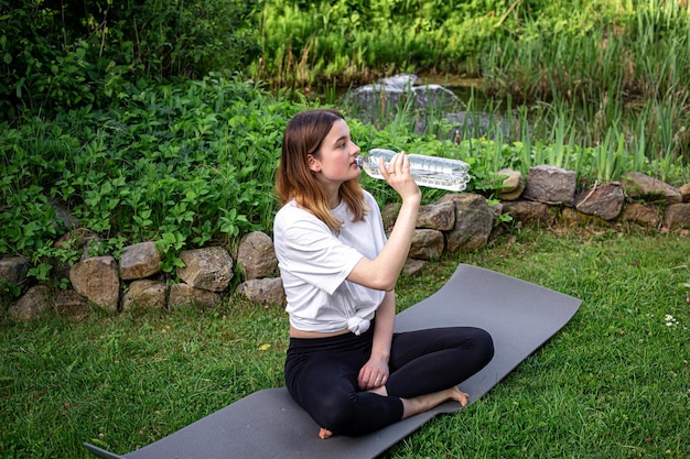 Uma jovem no tapete de fitness bebe água no conceito de esportes da natureza