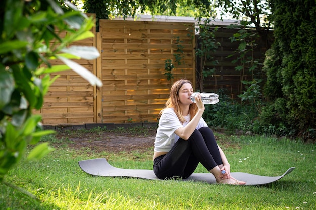 Uma jovem no tapete de fitness bebe água no conceito de esportes da natureza