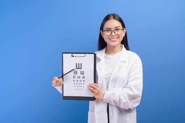 Uma jovem oftalmologista com óculos segurando o gráfico de olho sobre estúdio de fundo azul, conceito de saúde