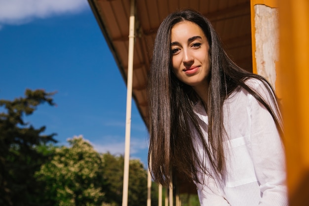 Foto uma jovem olha da varanda. o sol forte incide sobre a garota. linda menina morena aproveita o sol.