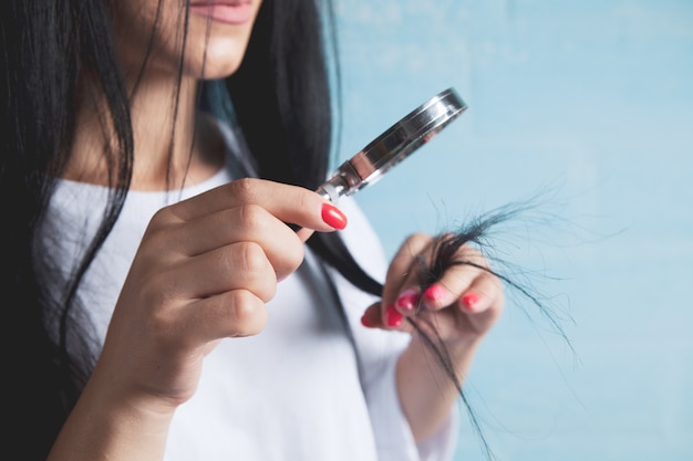 Uma jovem olha para o cabelo com uma lupa