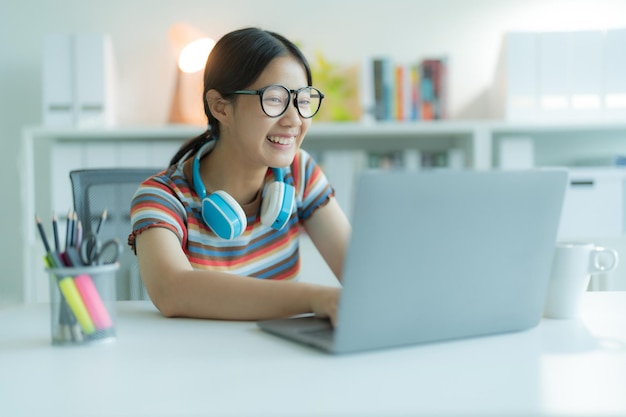 Foto uma jovem ou estudante usando um laptop na biblioteca enquanto usa óculos e fones de ouvido ela está sorrindo e parecendo feliz