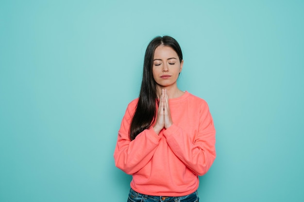 Uma jovem pacífica vestida de casual mantém as mãos em um gesto de oração e tem uma expressão calma