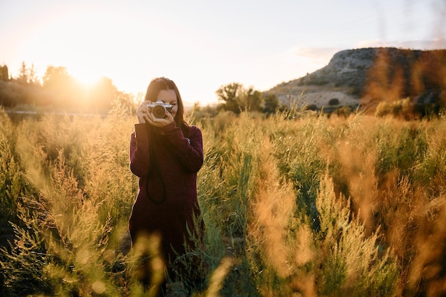 Uma jovem passeando pelo campo com sua câmera vintage ao pôr do sol