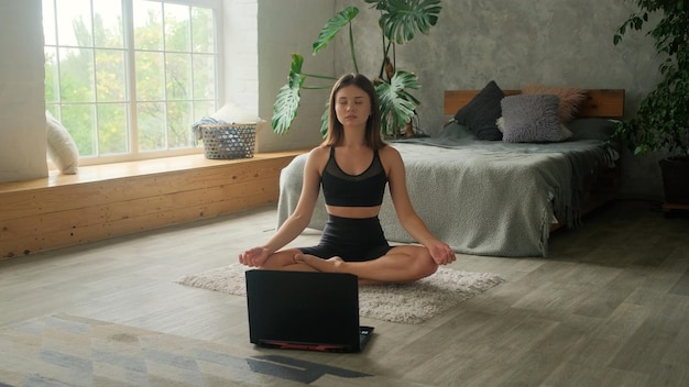 Foto uma jovem pratica exercícios online em casa. o laptop está no chão e a garota pratica esportes sozinha.