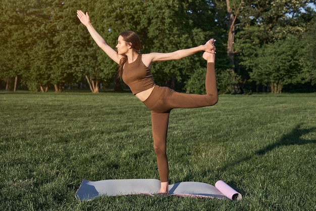 Uma jovem pratica ioga em um parque da cidade enquanto está em uma pose de guerreiro
