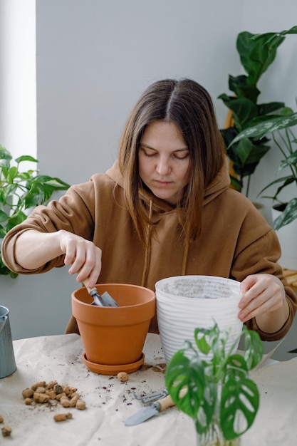 Uma jovem preparando um vaso de barro para envasar uma planta de casa, enchendo-a de solo usando pá