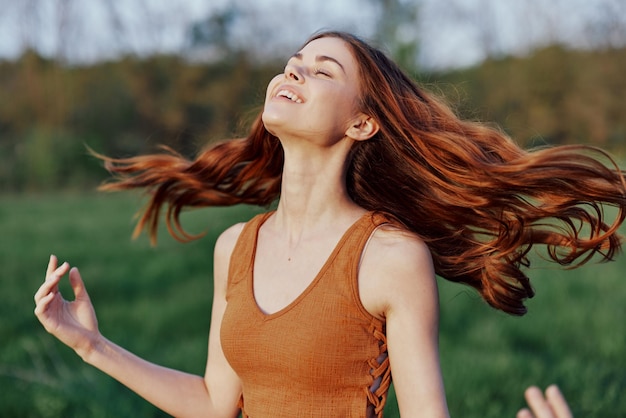 Uma jovem rindo e sorrindo alegremente na natureza no parque com a iluminação do pôr do sol iluminando seus longos cabelos ruivos