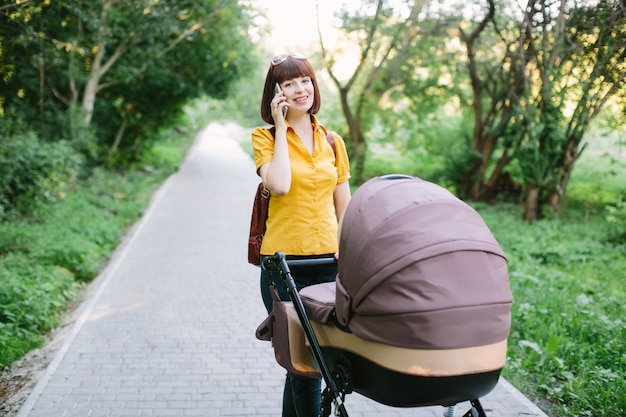 Uma jovem ruiva de camisa amarela está andando com um bebê pequeno no carrinho em um dia de verão no parque