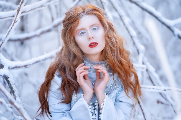 Uma jovem ruiva, uma princesa, caminha em uma floresta de inverno com um vestido gelo e neve nas árvores