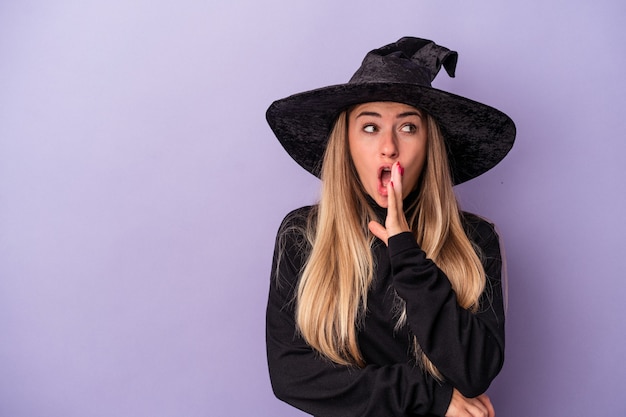 Foto uma jovem russa disfarçada de bruxa, comemorando o halloween, isolada em um fundo roxo, está contando uma notícia secreta de travagem e olhando para o lado