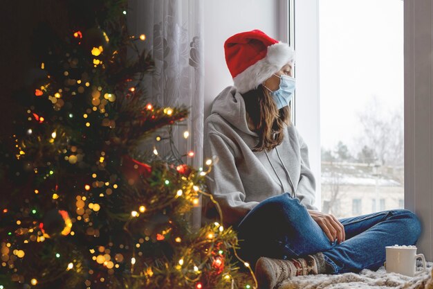 Uma jovem se senta à janela de uma casa decorada para o Natal, separa a janela