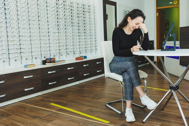 Foto uma jovem se senta e escolhe óculos em um salão de oftalmologia visão ruim