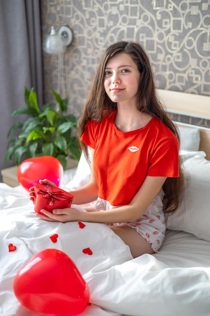 Uma jovem se senta na cama de manhã com um presente nas mãos Dia dos Namorados