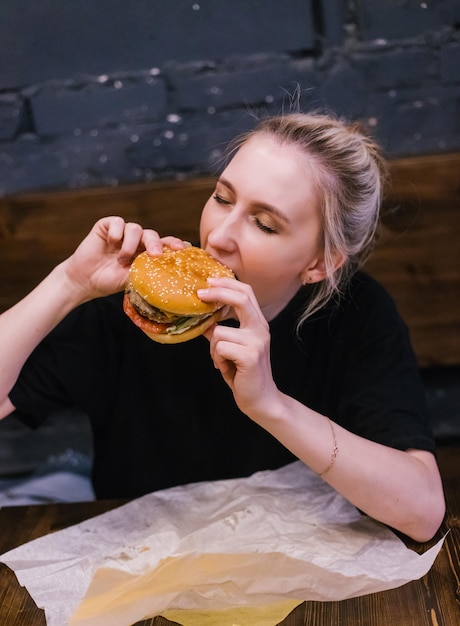 Uma jovem segura um hambúrguer com um hambúrguer de carne nas mãos Almoço delicioso e saudável Fast food e lanches