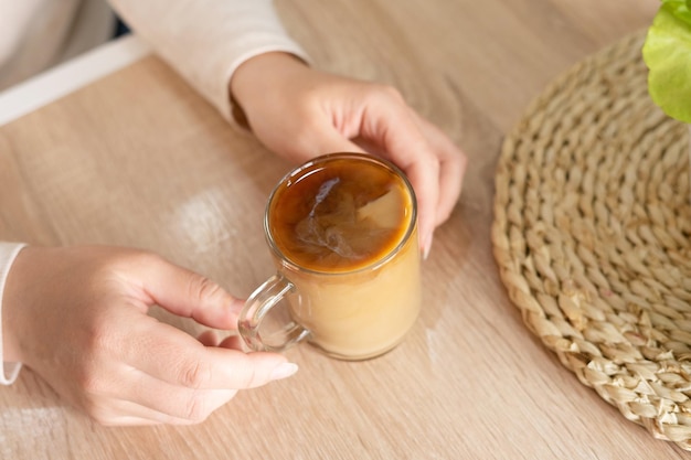 Uma jovem segura uma caneca de café com leite nas mãos enquanto está sentada em uma mesa com potes de verduras Café da dona de casa