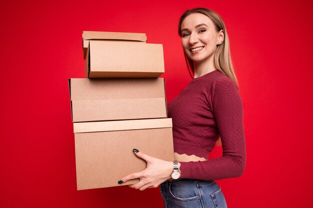 Uma jovem segurando caixas de papelão em um fundo vermelho