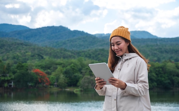 Uma jovem segurando e usando tablet digital enquanto viaja montanhas e lago